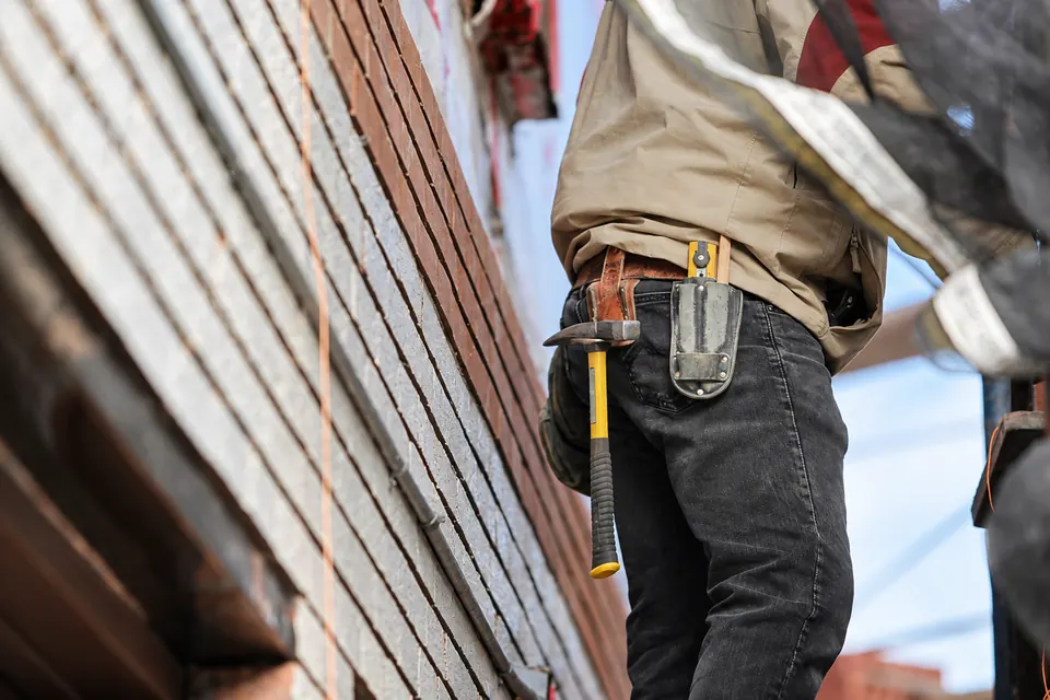 Construction worker carrying a tool belt beside a brick wall